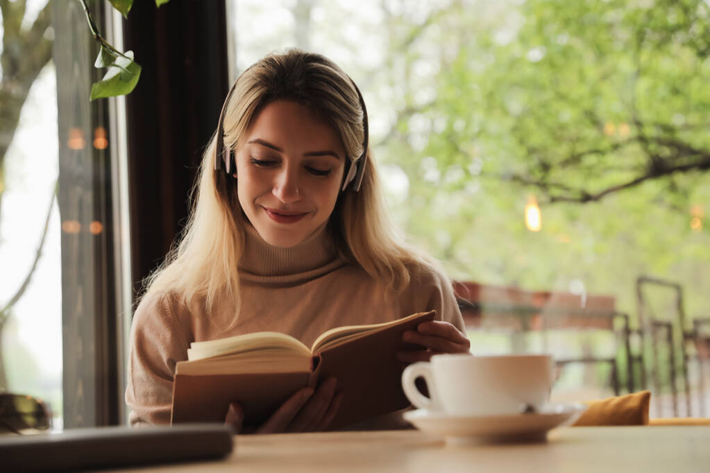 Жінка слухає аудіокнигу за столом у кафе
 - Фото, зображення
