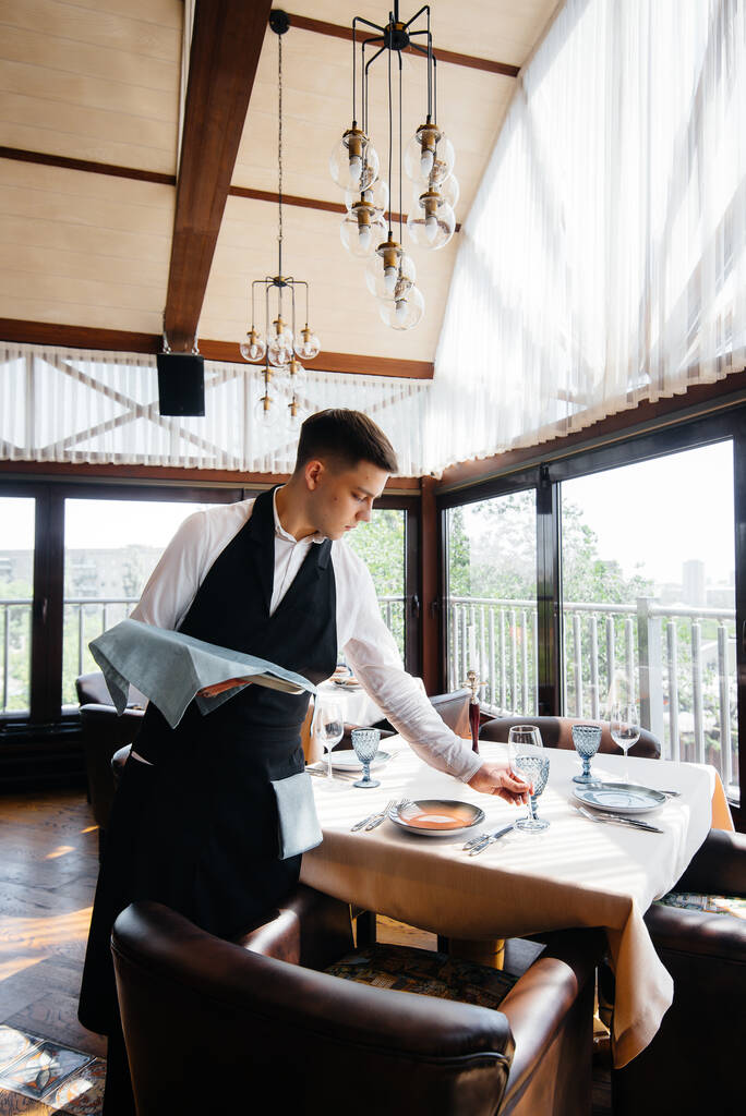 Un giovane cameriere in uniforme elegante è impegnato a servire il tavolo in un bellissimo ristorante gourmet. Attività di ristorazione, di altissimo livello. - Foto, immagini