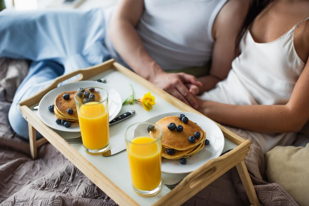 snídaně tác s palačinkami a pomerančový džus v blízkosti pár v posteli - Fotografie, Obrázek