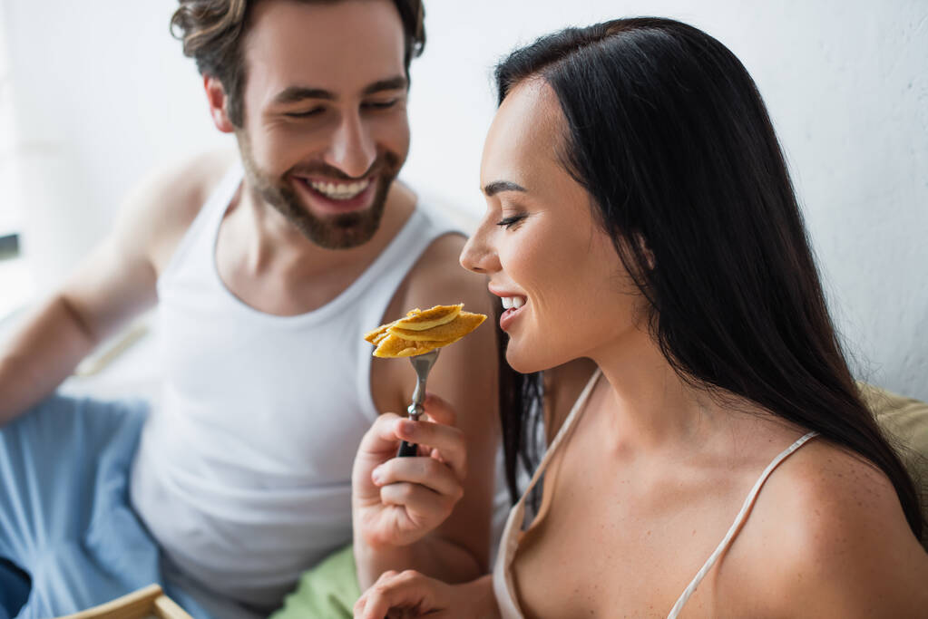 homem alegre alimentando namorada com panquecas saborosas  - Foto, Imagem
