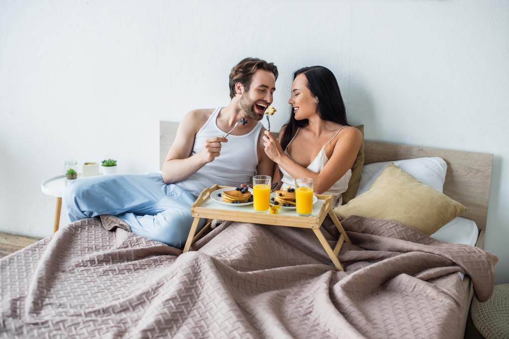 femme gaie nourrissant petit ami avec des crêpes savoureuses au lit - Photo, image
