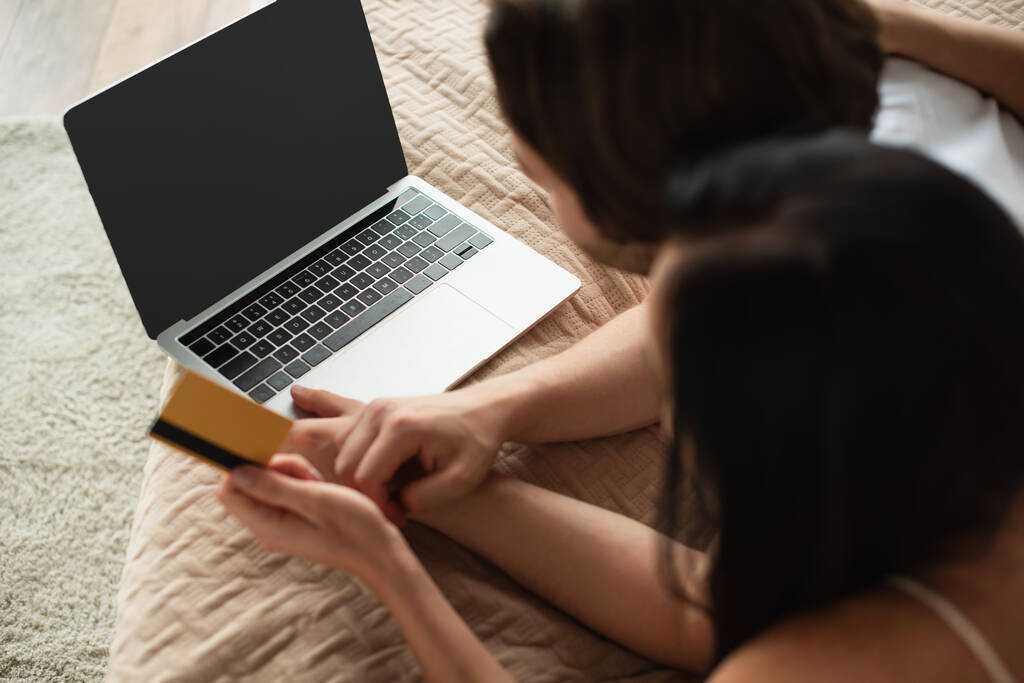 ベッドルームでオンラインショッピングをしながらノートパソコンの近くにクレジットカードを持っているカップルの高い角度のビュー - 写真・画像