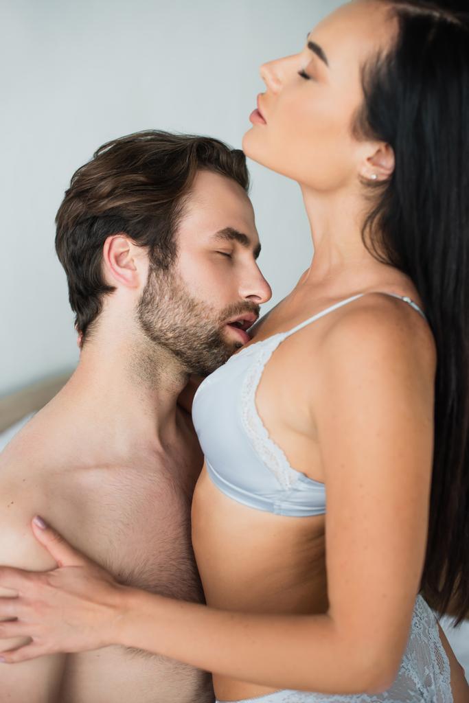 bärtiger Mann küsst brünette Frau im BH mit geschlossenen Augen - Foto, Bild