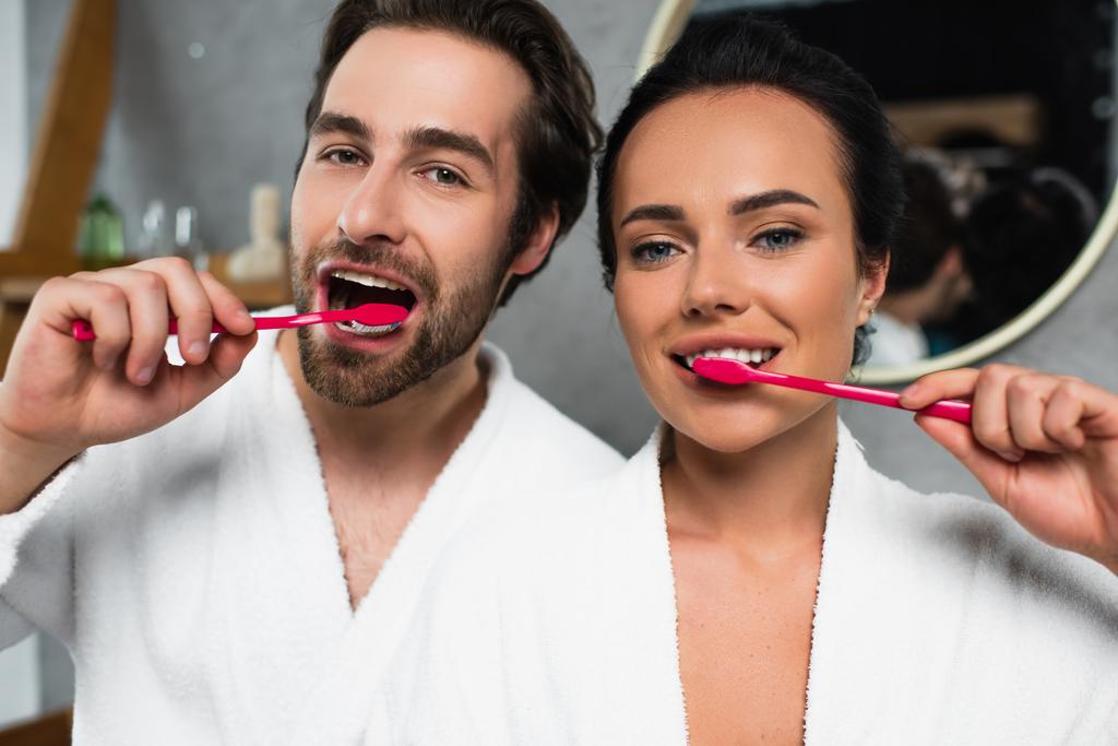 feliz pareja joven en batas blancas cepillarse los dientes - Foto, imagen