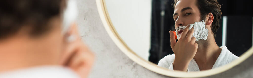 mężczyzna nakładający piankę do golenia na twarz przy lustrze, baner - Zdjęcie, obraz