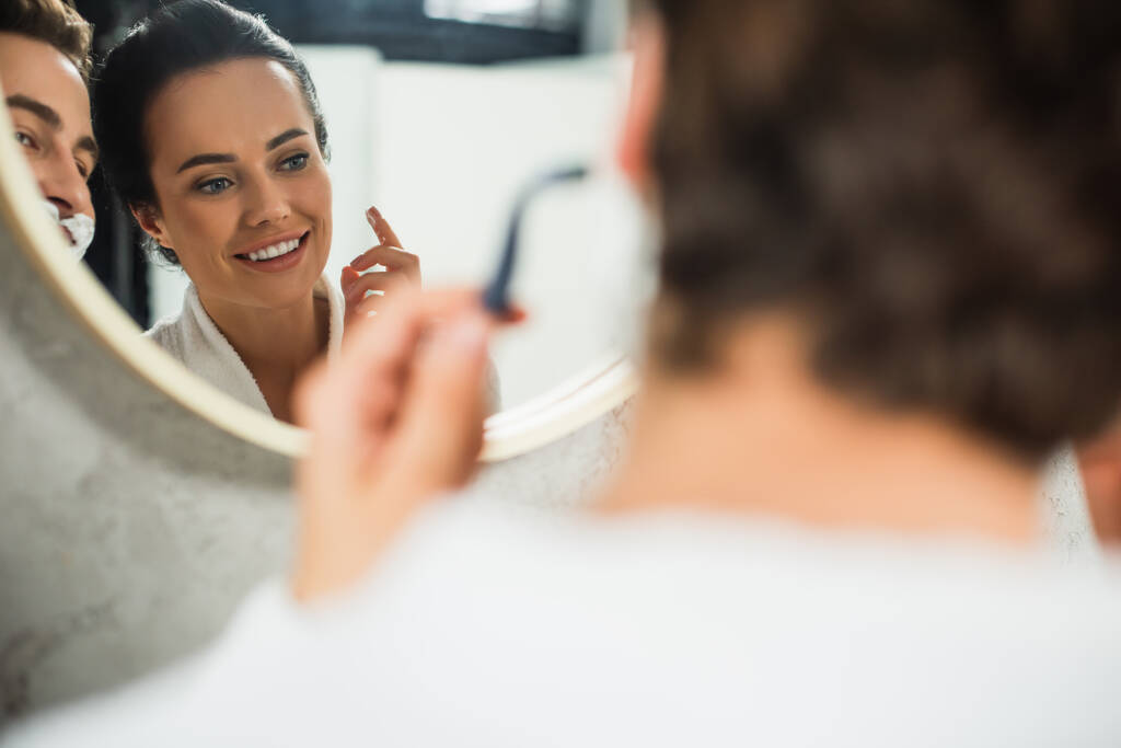 バスルームで男の髭剃りを見て幸せな女性の鏡に映る - 写真・画像