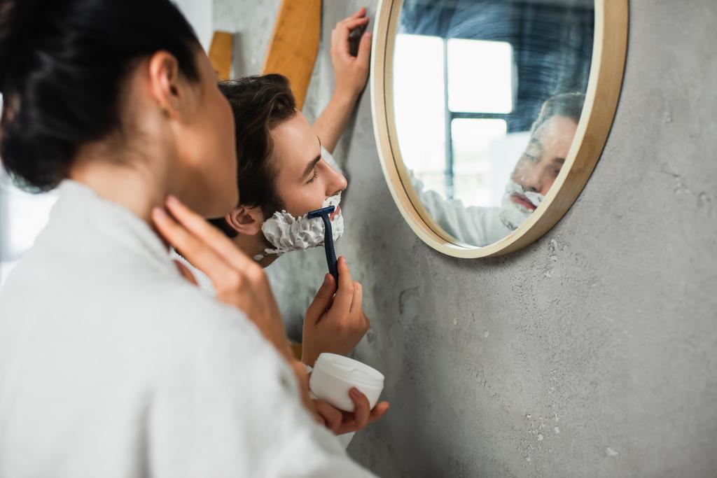 hombre afeitándose cerca borrosa novia en cuarto de baño  - Foto, imagen