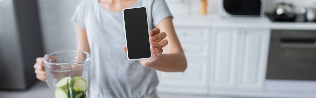 περικοπή άποψη του θολή γυναίκα δείχνει smartphone με λευκή οθόνη κοντά αναδευτήρα με κολοκυθάκια, banner - Φωτογραφία, εικόνα