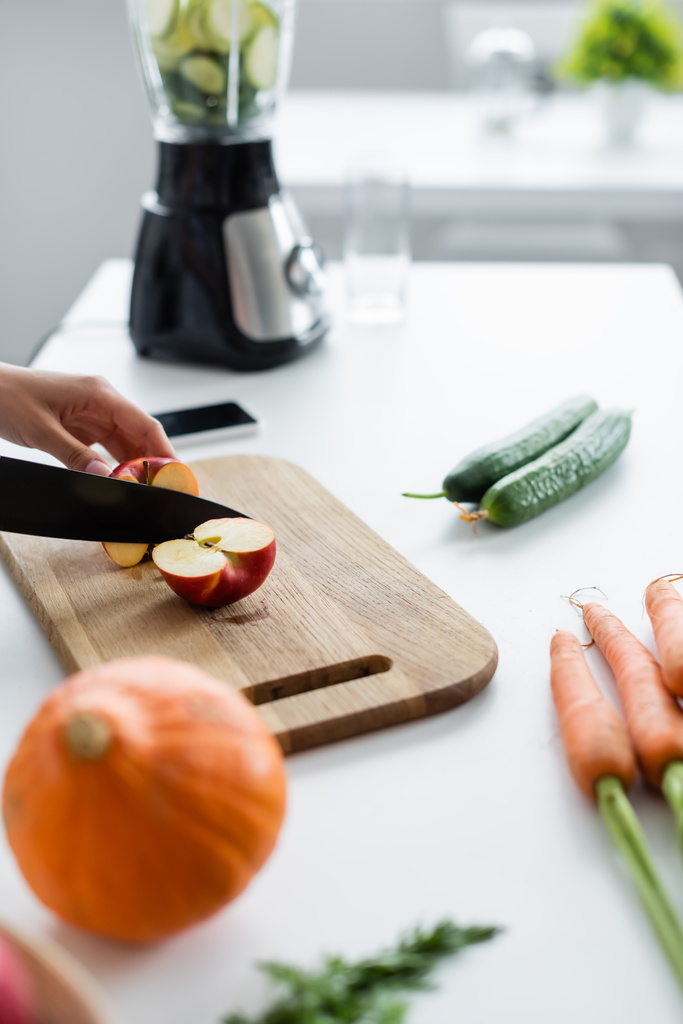 vista parcial de la mujer cortando manzana cerca de calabaza borrosa y zanahorias en la mesa - Foto, Imagen