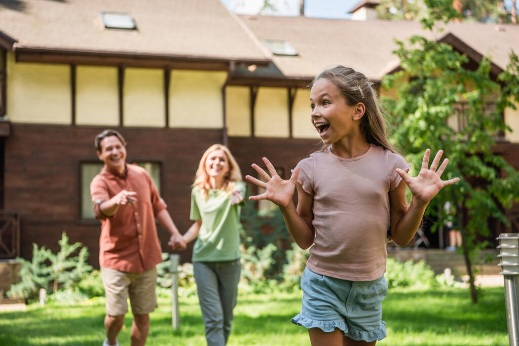 Позитивный ребенок стоит рядом с родителями и размытый дом отдыха  - Фото, изображение