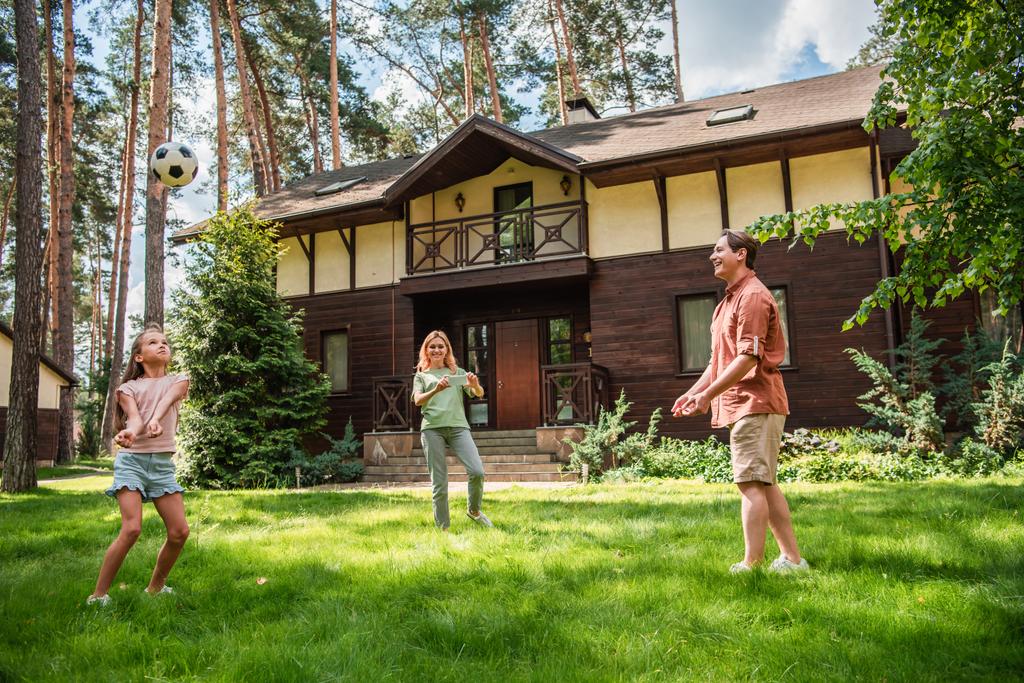 Позитивная семья играет в волейбол на лужайке возле дома отдыха  - Фото, изображение