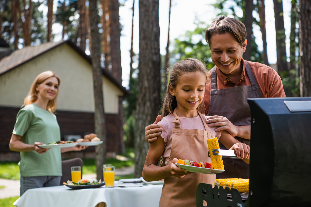 Mosolygó apa mellett áll lánya gazdaság kukorica és zöldségek piknik közben  - Fotó, kép