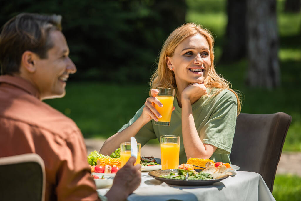 Mosolygó nő narancslével ül közel férj és az élelmiszer a szabadban  - Fotó, kép