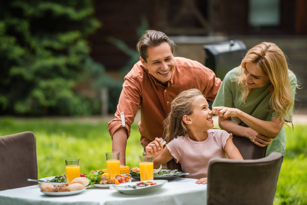 Familia alegre cerca de la comida sabrosa durante el picnic al aire libre  - Foto, Imagen