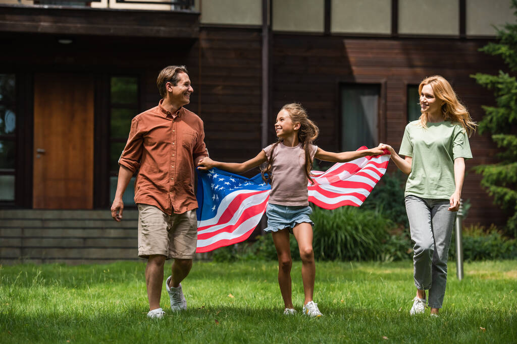 Kid with american flag holding hands of parents on lawn  - Foto, afbeelding