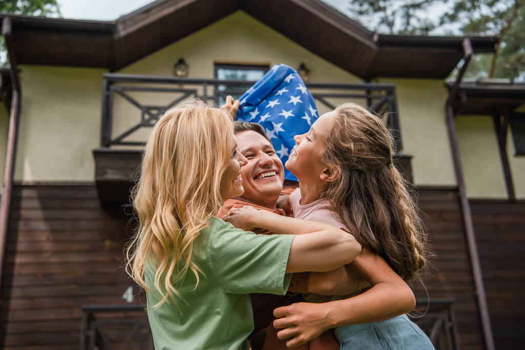 Family with american flag hugging outdoors during weekend  - Foto, afbeelding