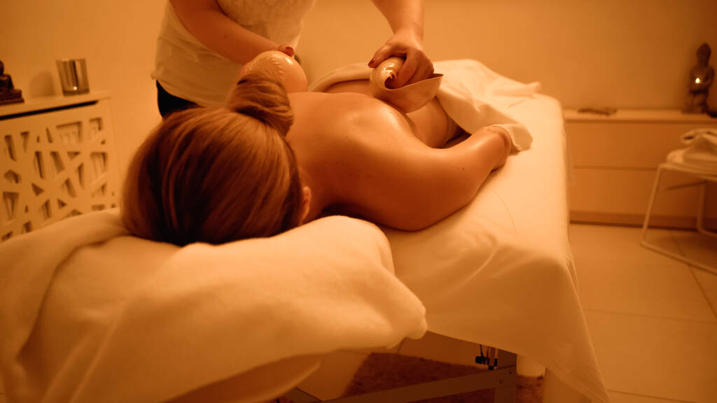professioneller Masseur massiert junge Frau mit Muscheln im Wellness-Salon  - Foto, Bild