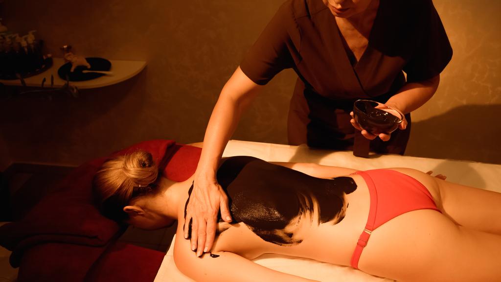 massaggiatore che applica il fango sul corpo di giovane donna sul tavolo da massaggio - Foto, immagini