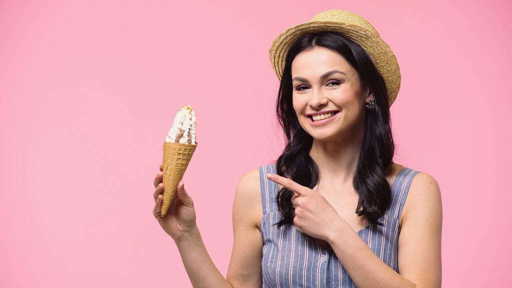 Brune femme au chapeau de soleil pointant vers la crème glacée isolée sur rose  - Photo, image