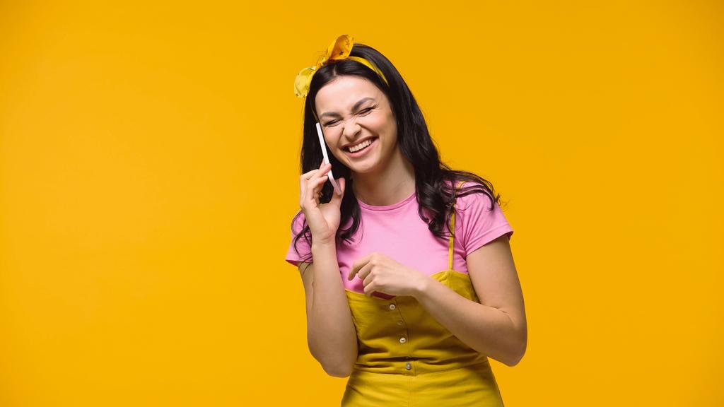 Donna eccitata con gli occhi chiusi ridendo mentre parla su smartphone isolato sul giallo - Foto, immagini