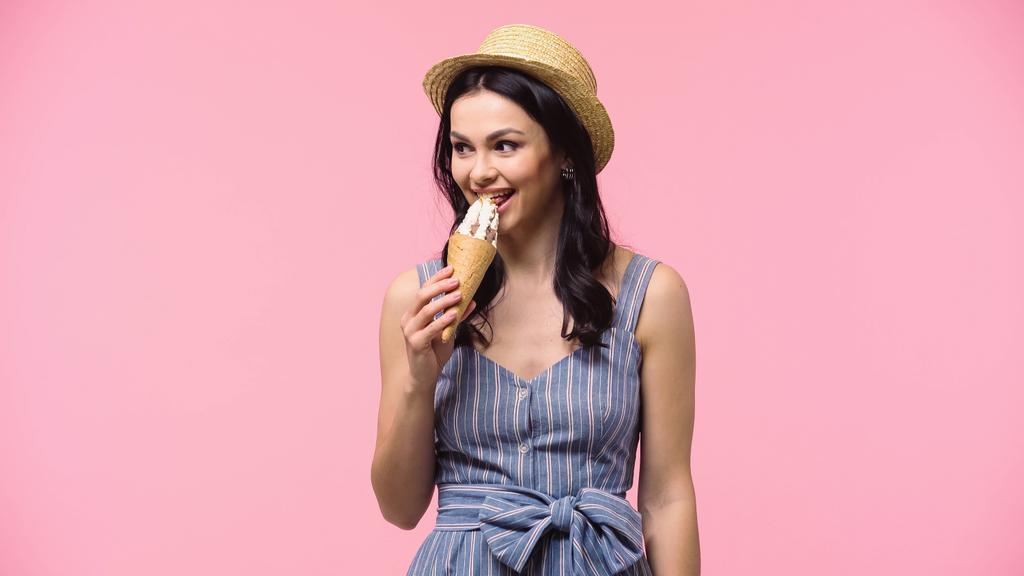 Femme au chapeau de soleil mangeant de la crème glacée isolée sur rose  - Photo, image