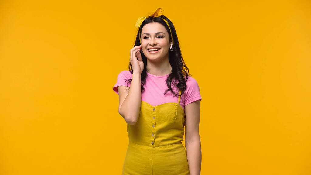 黄色に隔離された無線イヤフォンの陽気な女性  - 写真・画像
