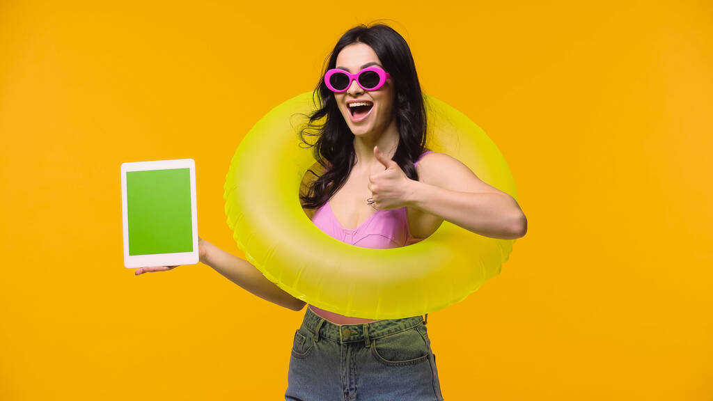 Mujer emocionada con anillo de natación y tableta digital que muestra como aislado en amarillo  - Foto, Imagen