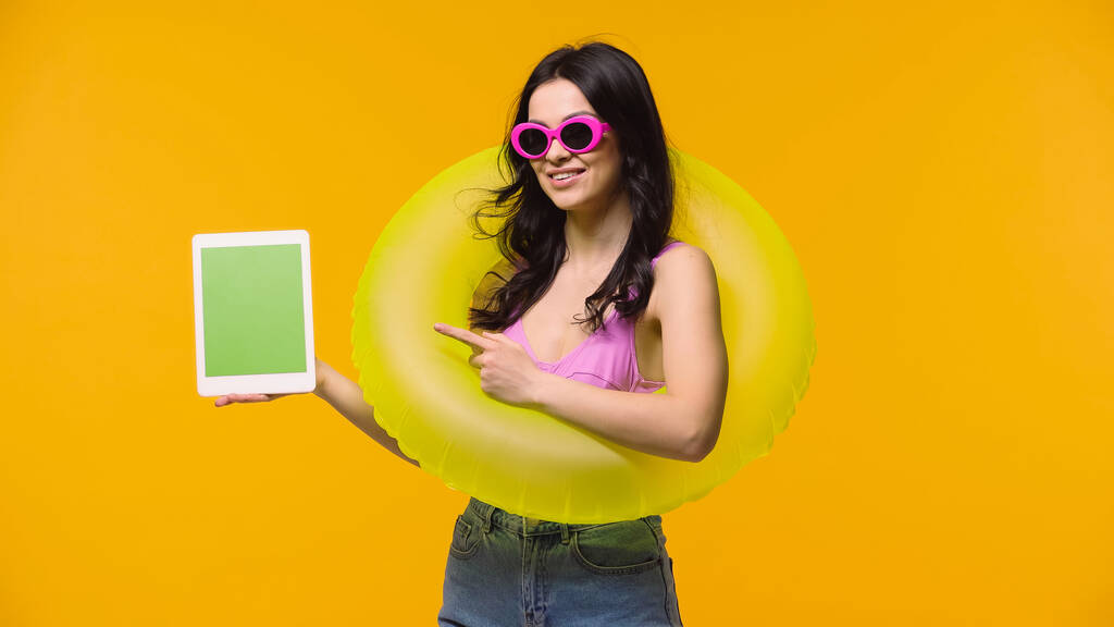 Žena v plavkách a plaveckém kroužku ukazuje na digitální tablet s chroma klíčem izolovaným na žluté  - Fotografie, Obrázek