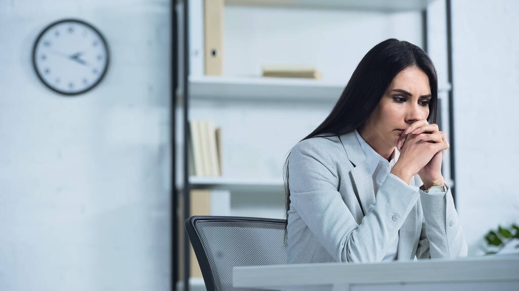 worried businesswoman with clenched hands sitting at desk  - Photo, Image