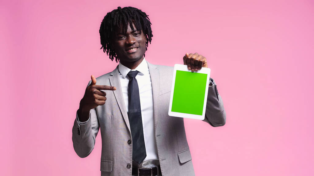 allegro uomo d'affari afroamericano che punta al tablet digitale isolato su rosa - Foto, immagini
