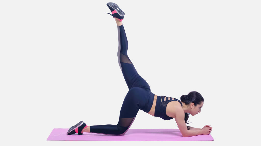 volledige lengte van jonge vrouw in sportkleding stretching op roze fitness mat op wit - Foto, afbeelding