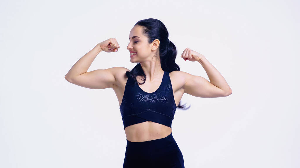 glimlachende sportvrouw tonen spieren geïsoleerd op wit - Foto, afbeelding