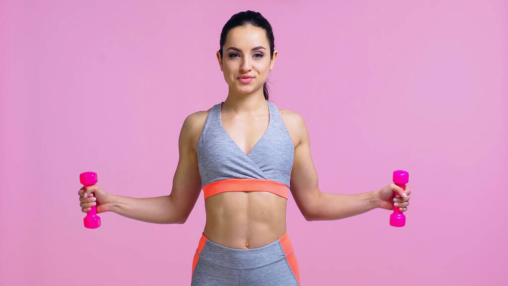 pleased young woman working out with dumbbells isolated on pink - Photo, Image