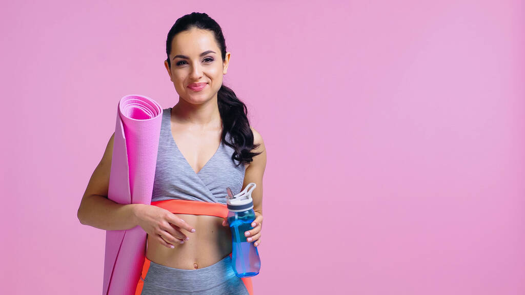 szczęśliwy sportowiec gospodarstwa sportowe butelki i fitness maty izolowane na różowy - Zdjęcie, obraz