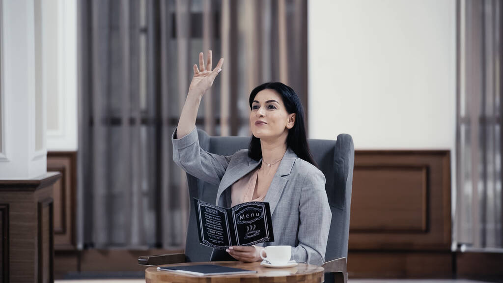happy businesswoman holding menu and gesturing in lobby of restaurant - Photo, image