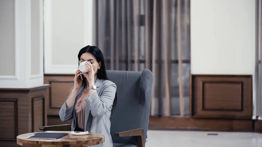 Bizneswoman rozmawia na smartfonie i pije kawę w lobby restauracji - Zdjęcie, obraz
