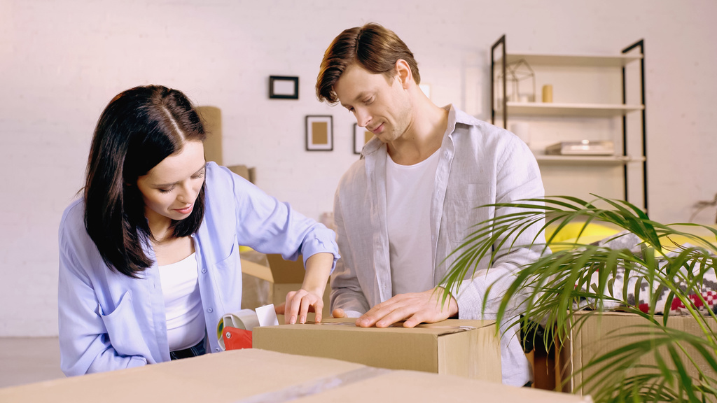 pareja joven utilizando cinta adhesiva mientras que la caja de embalaje - Foto, Imagen