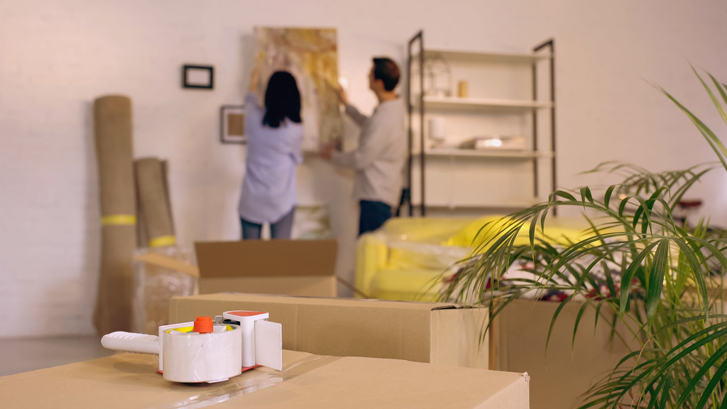cinta adhesiva en cajas cerca borrosa pareja colgando pintura en un nuevo hogar - Foto, Imagen