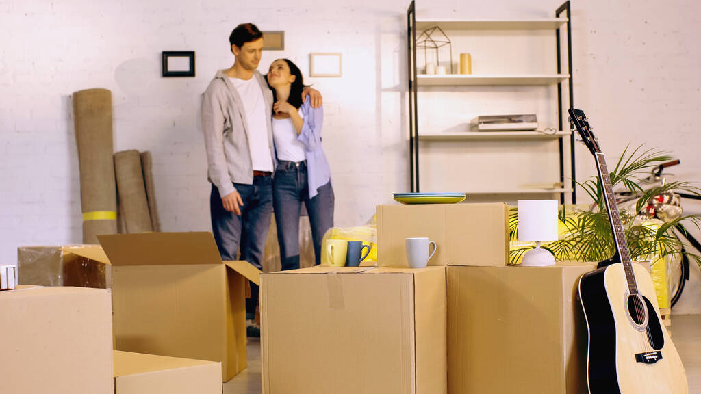 homme flou étreignant petite amie heureuse près de boîtes en carton dans une nouvelle maison   - Photo, image