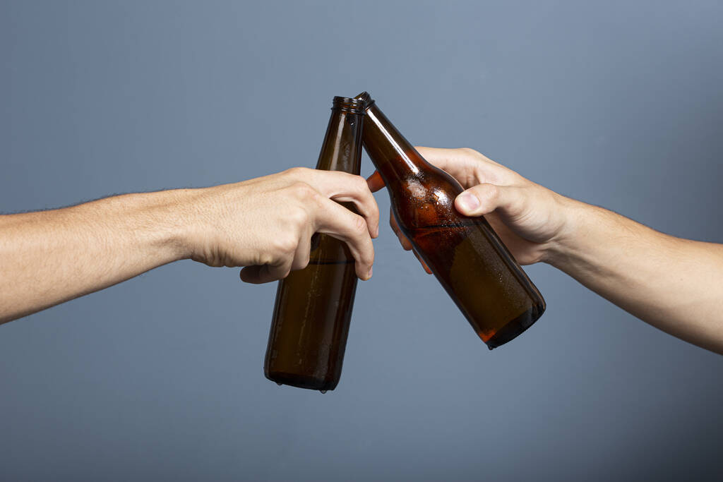 Dos amigos aferrándose a botellas de cerveza; tiro de manos - Foto, Imagen