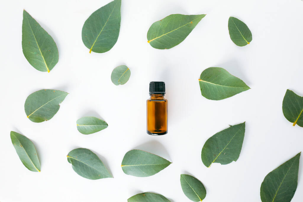 Un primer plano de 1 ml de vial de aceite esencial de ámbar y hojas verdes aisladas sobre un fondo blanco - Foto, imagen