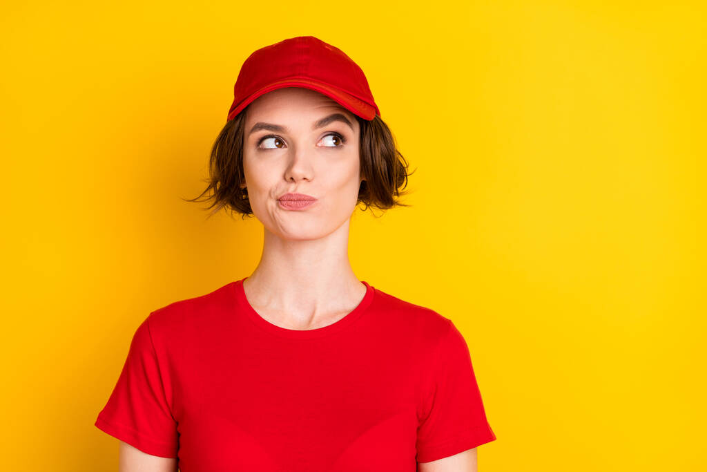 Fotografie rozkošný přemýšlivý mladý doručit dáma červená pracovní oděv čepice hledá prázdný prostor izolované žlutá barva pozadí - Fotografie, Obrázek