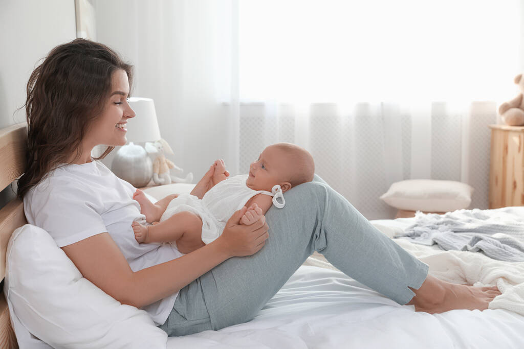 Felice giovane madre con il suo bambino carino sul letto a casa - Foto, immagini
