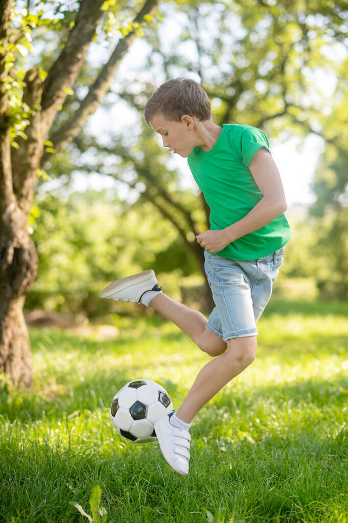 Boy jumping with soccer ball in nature - Photo, Image