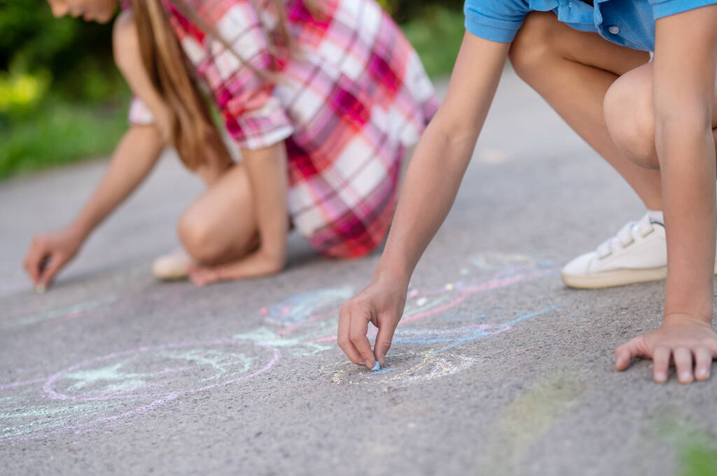 Las manos de los niños dibujando con lápices de colores sobre asfalto - Foto, imagen