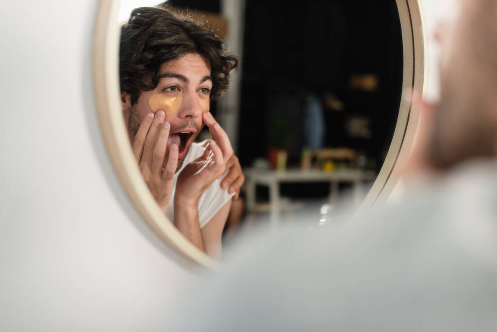 homosexual hombre aplicando parches en los ojos y mirando el espejo - Foto, Imagen