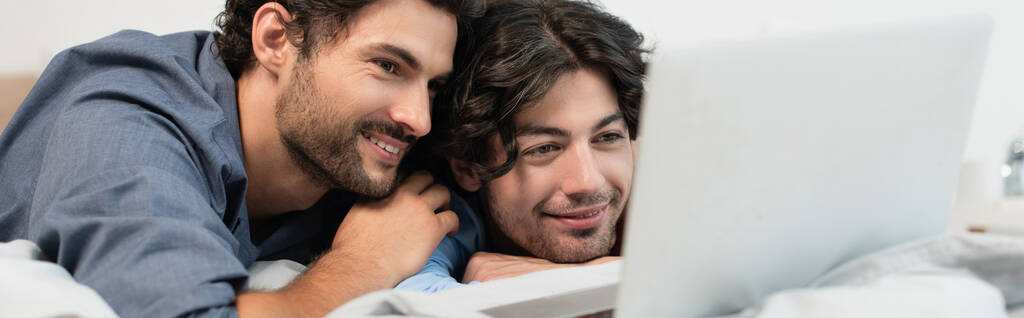 feliz pareja gay viendo película en el ordenador portátil en el dormitorio, bandera - Foto, imagen