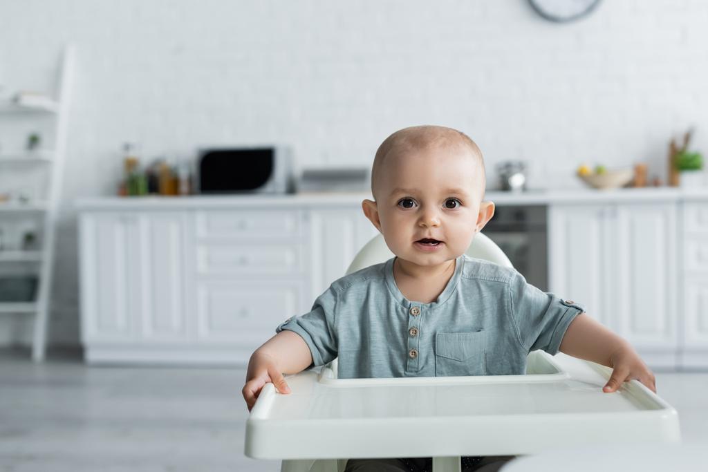 Bébé fille regardant caméra sur chaise haute à la maison  - Photo, image