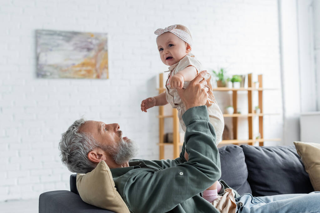 Starší otec drží pláč dítě na gauči  - Fotografie, Obrázek