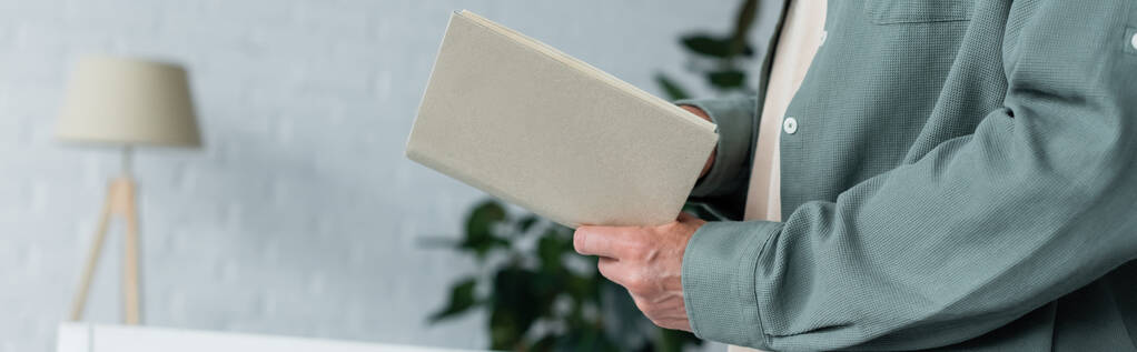 Обрезанный вид человека, держащего книгу дома, баннер  - Фото, изображение
